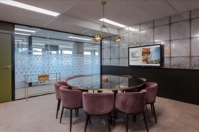 Salle de réunion moderne avec table en marbre, chaises bleues, écran mural et cloison vitrée décorative.
