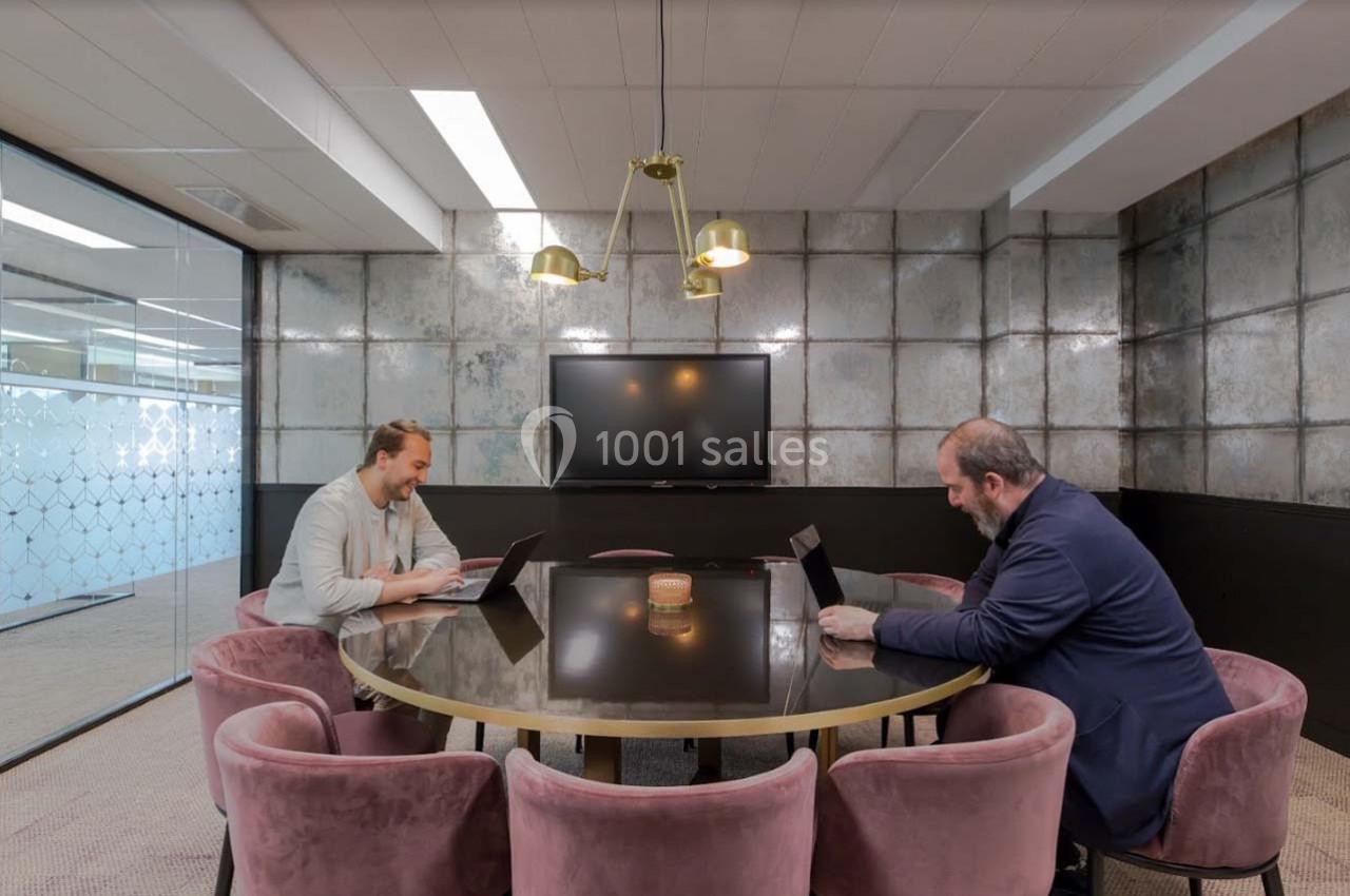 Deux hommes travaillent sur des ordinateurs portables autour d'une table ronde dans une salle de réunion moderne.