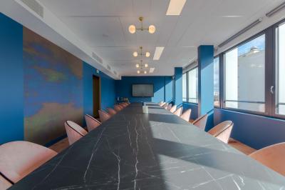 Salle de réunion moderne avec table en marbre, chaises bleues, écran mural et cloison vitrée décorative.