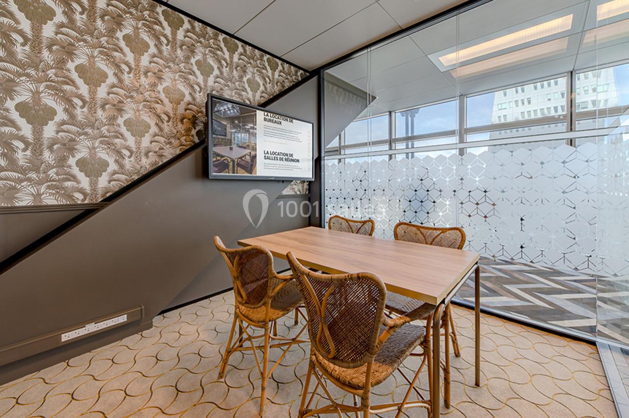 Salle de réunion avec table en bois, chaises en rotin, mur décoré de motifs végétaux et cloison vitrée partiellement opaque.