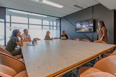 Deux personnes discutent dans une salle de réunion moderne avec écran mural et mobilier haut.
