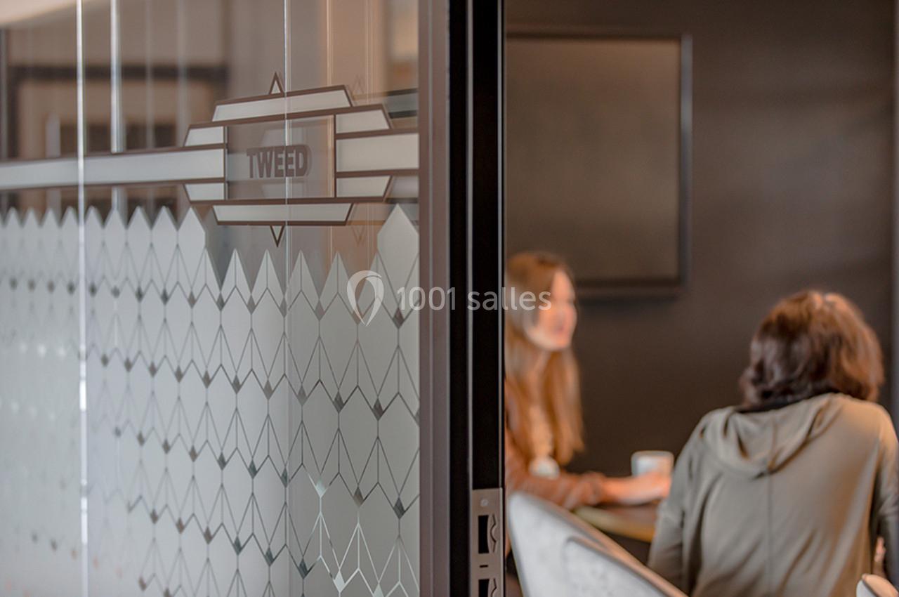 Deux personnes discutent dans une salle de réunion aux parois vitrées décorées de motifs géométriques.