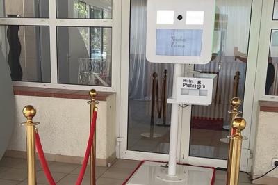 Salle de réception décorée pour un mariage, avec tables dressées, fleurs blanches et rouges, et arche florale en arrière…