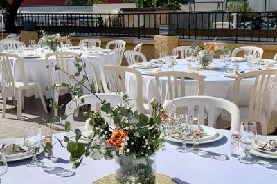 Salle de réception décorée pour un mariage, avec tables dressées, fleurs blanches et rouges, et arche florale en arrière…