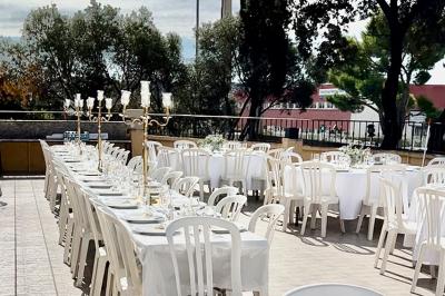Salle de réception décorée pour un mariage, avec tables dressées, fleurs blanches et rouges, et arche florale en arrière…