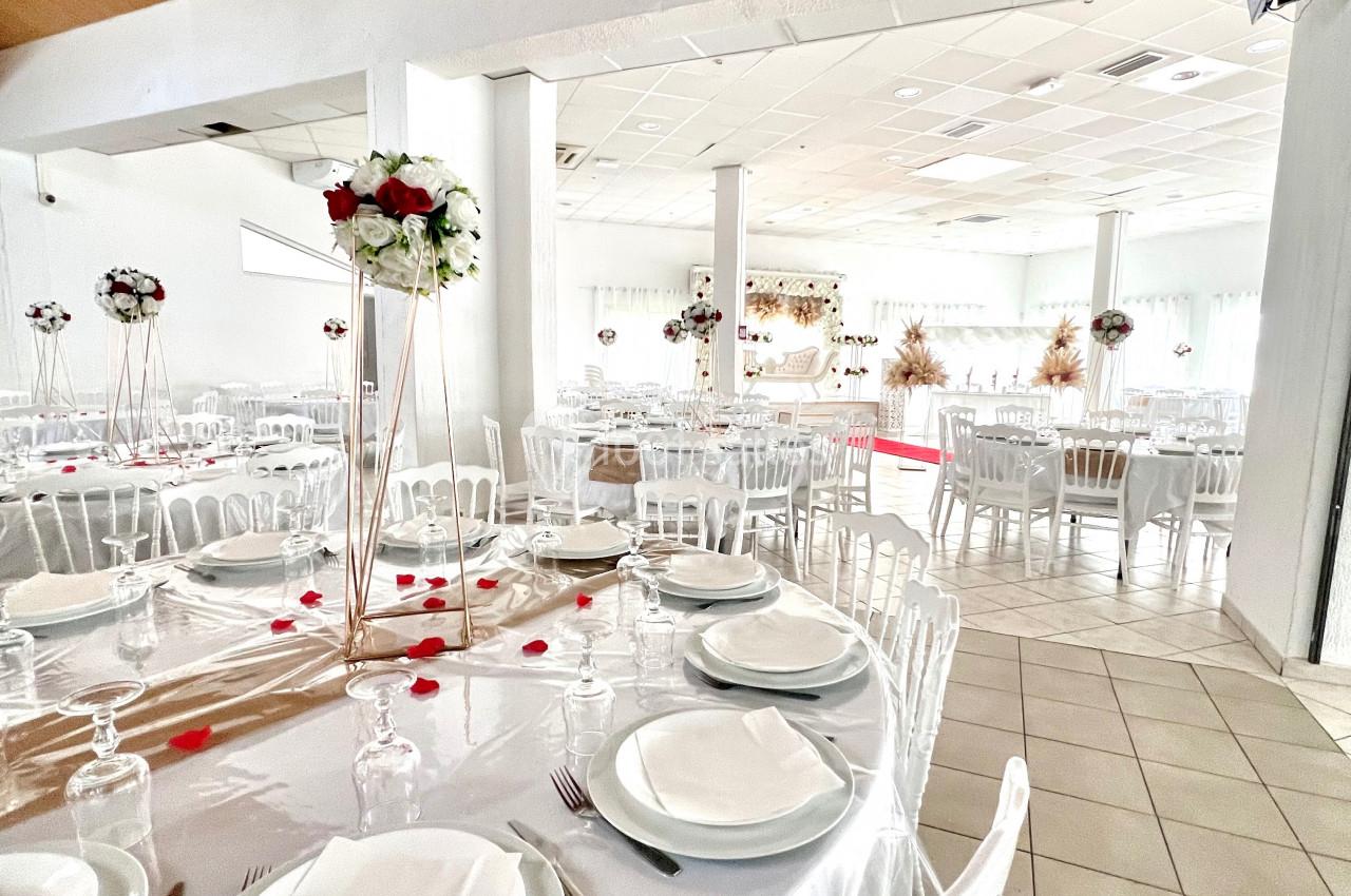 Salle de réception décorée avec des tables rondes dressées, nappes blanches et centres de table fleuris.