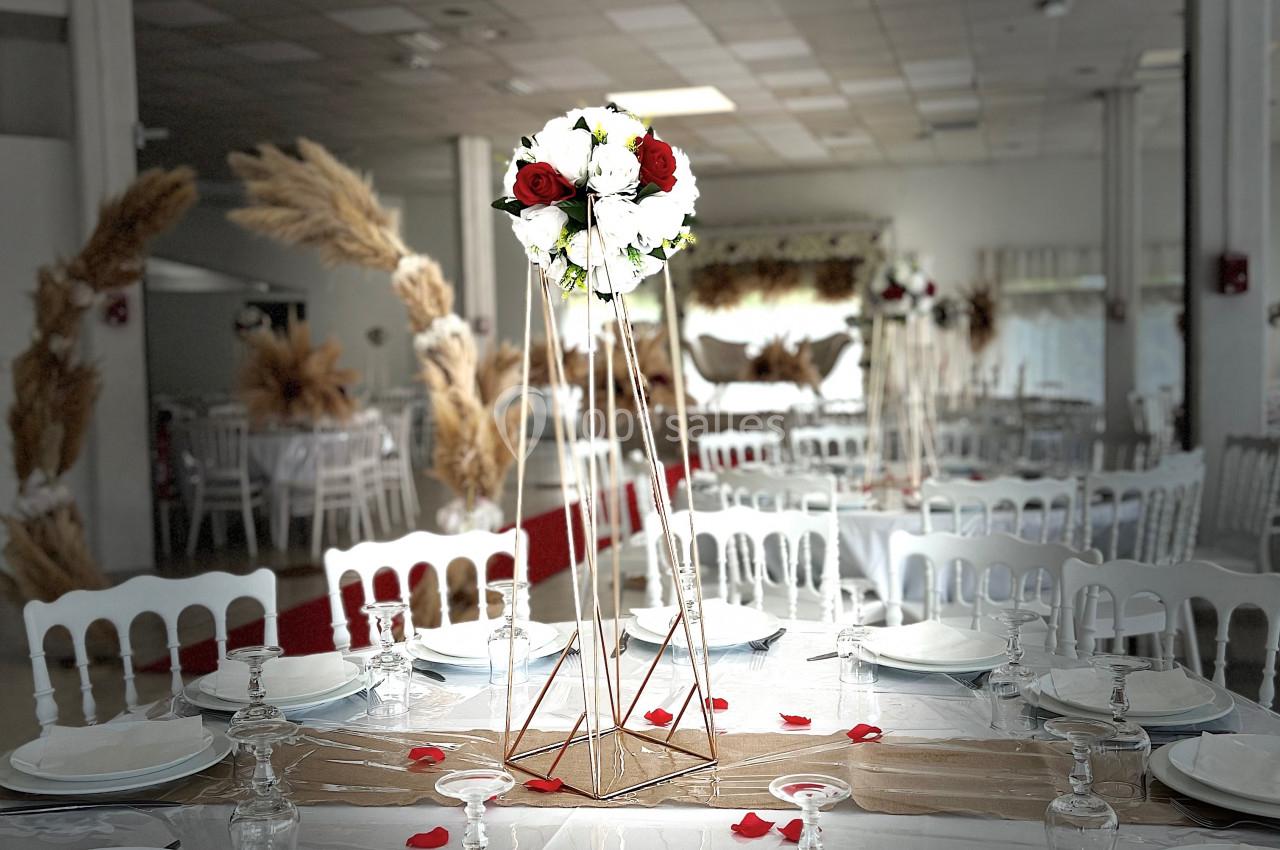 Salle de réception décorée avec des tables dressées, un centre de table floral et des éléments en pampas en arrière-plan.