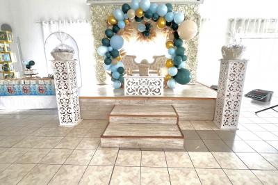 Salle de réception décorée pour un mariage, avec tables dressées, fleurs blanches et rouges, et arche florale en arrière…