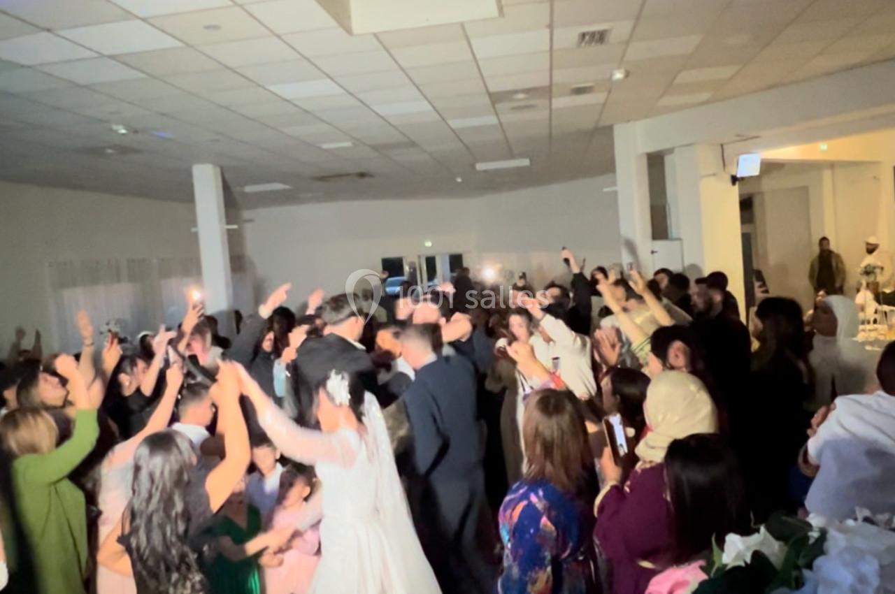Des invités dansent et célèbrent dans une salle de réception éclairée, avec une mariée en robe blanche au premier plan.