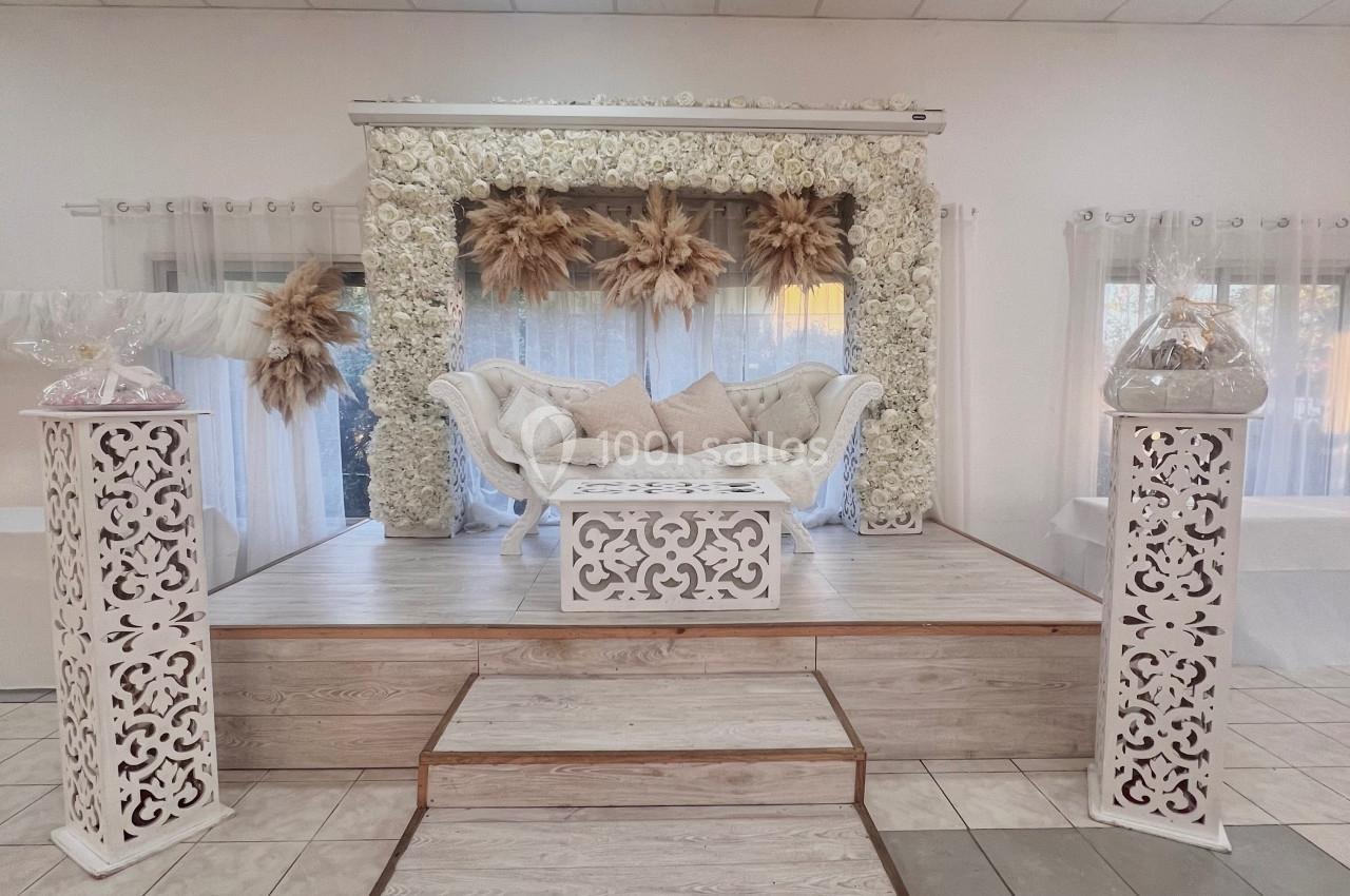 Estrade décorée avec un canapé blanc, des fleurs séchées et des éléments floraux sous un dais lumineux.