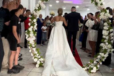 Salle de réception décorée pour un mariage, avec tables dressées, fleurs blanches et rouges, et arche florale en arrière…