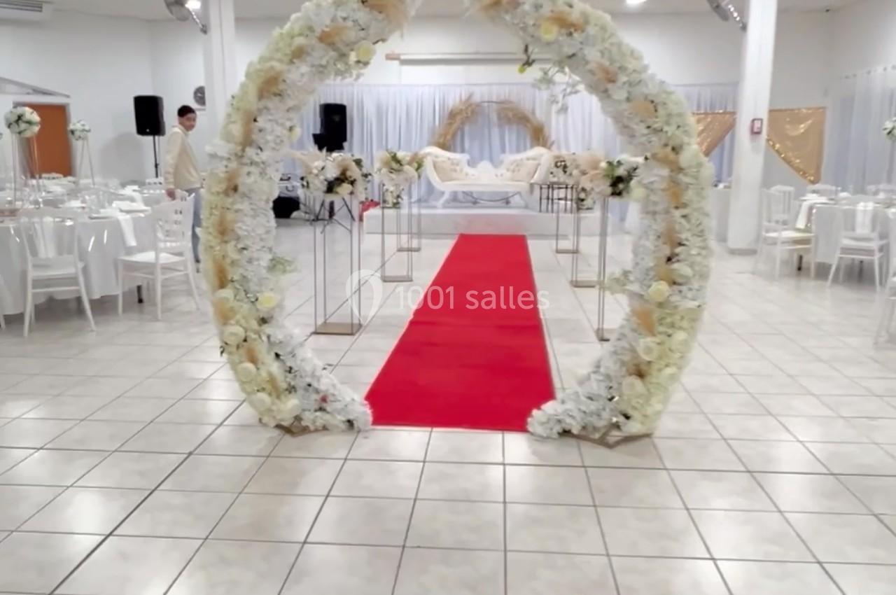 Arche florale blanche entourant un tapis rouge dans une salle de réception décorée pour un événement.