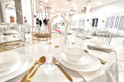 Salle de réception décorée pour un mariage, avec tables dressées, fleurs blanches et rouges, et arche florale en arrière…