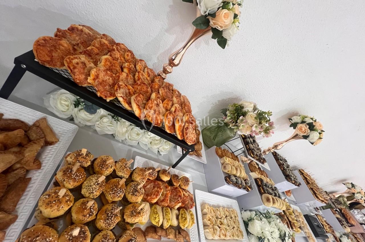 Buffet composé de viennoiseries salées, pains garnis et décorations florales sur une table blanche.