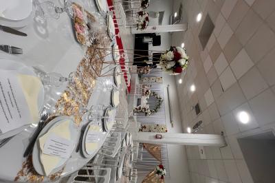 Salle de réception décorée pour un mariage, avec tables dressées, fleurs blanches et rouges, et arche florale en arrière…