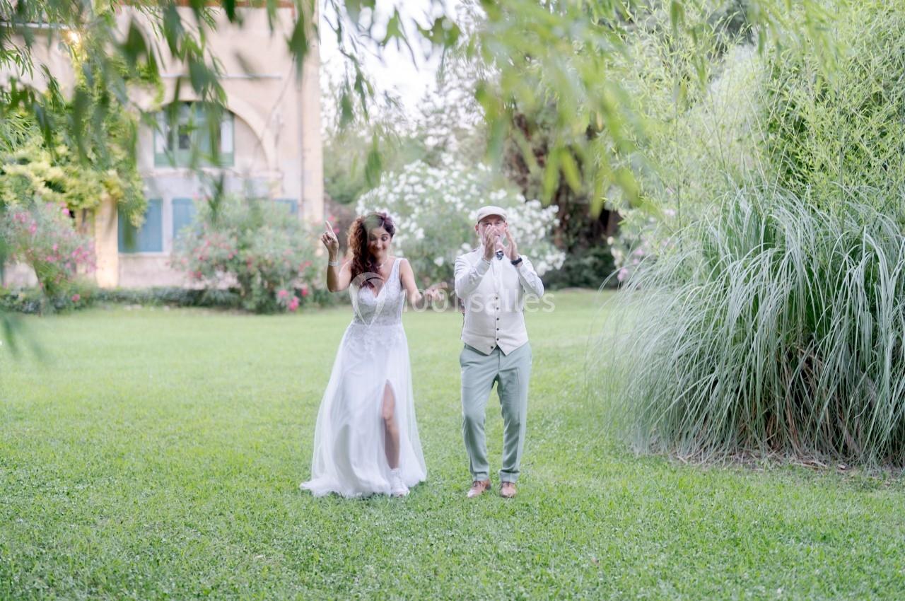 Un couple en tenue de mariage danse sur une pelouse entourée de végétation et d'un bâtiment en arrière-plan.