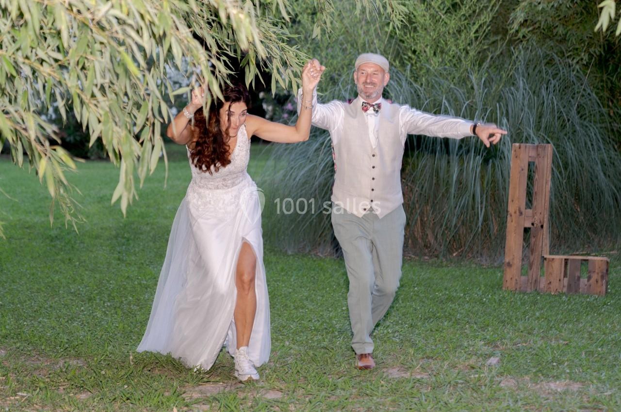 Un couple en tenue de mariage danse joyeusement sur une pelouse entourée de végétation.