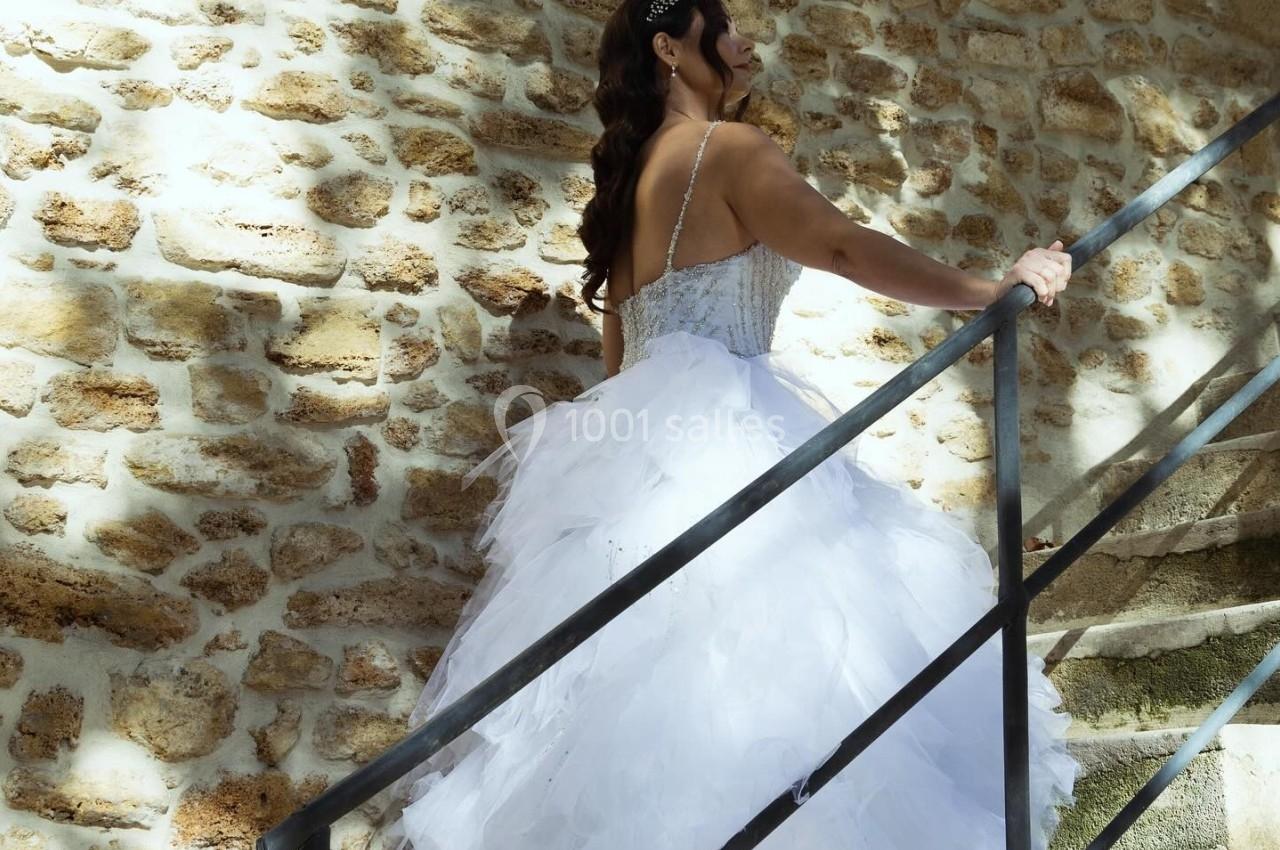 Femme en robe de mariée blanche montant un escalier en pierre, éclairée par une lumière naturelle.