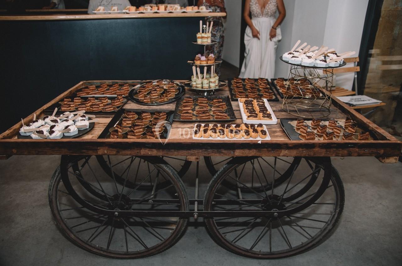 Table en bois sur roues présentant un assortiment de desserts variés disposés sur des plateaux et supports.