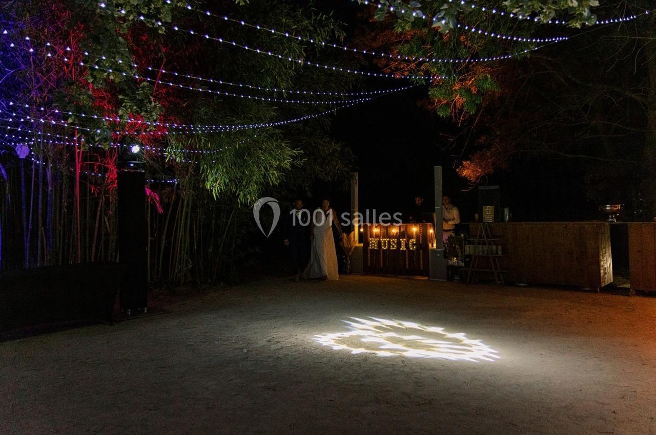 Un espace extérieur décoré de guirlandes lumineuses avec une piste éclairée et des invités en arrière-plan.