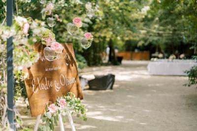 Chambre lumineuse avec lit double, commode en bois, portant à vêtements, télévision et poutre apparente au plafond.