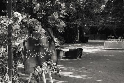 Chambre lumineuse avec lit double, commode en bois, portant à vêtements, télévision et poutre apparente au plafond.