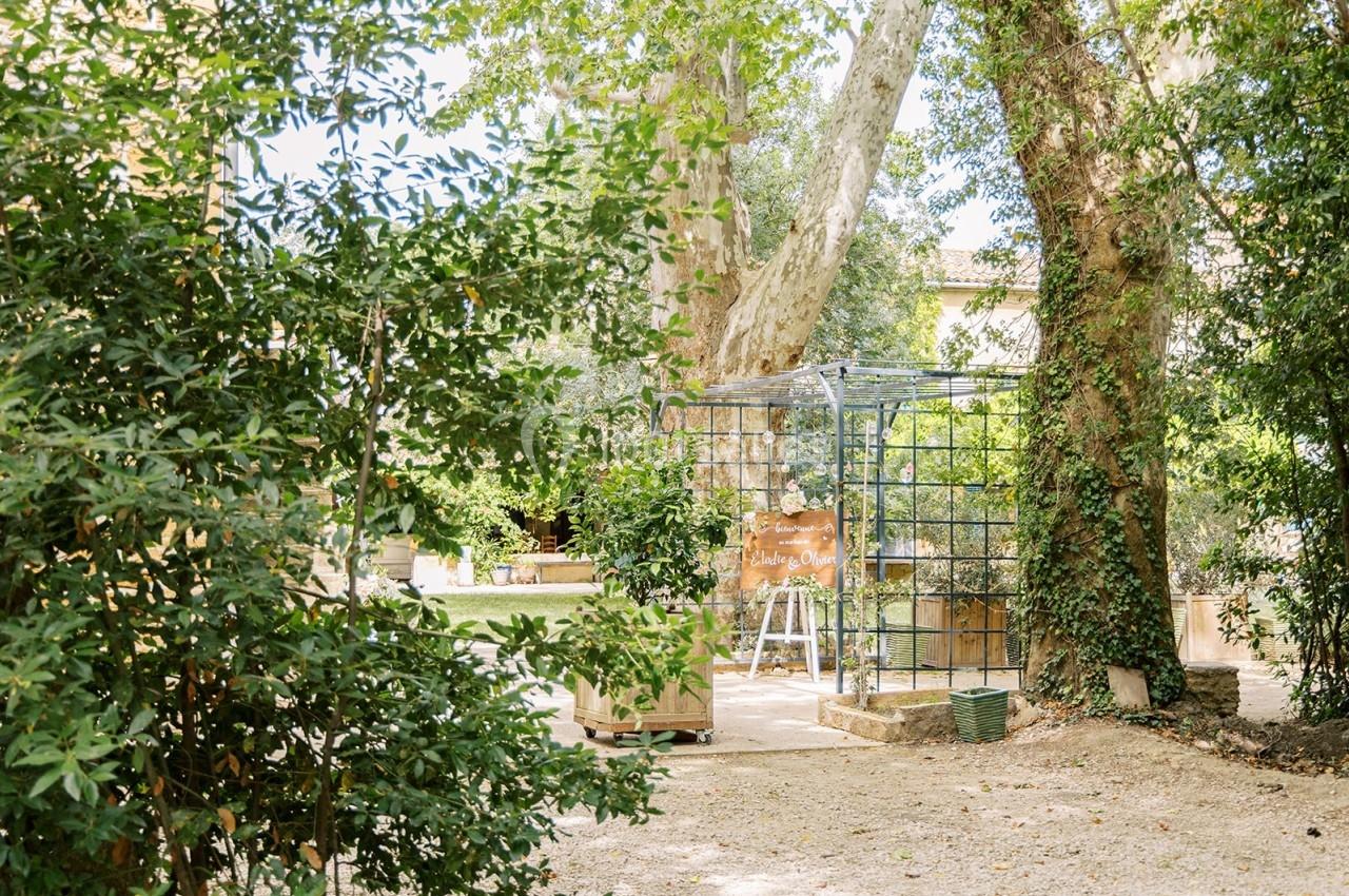 Jardin ombragé avec une structure métallique décorative entourée de végétation et d'arbres imposants.