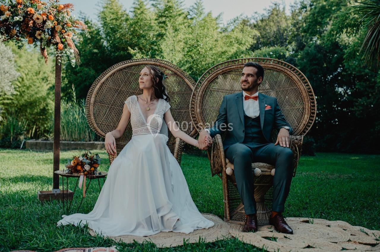 Un couple assis sur des fauteuils en osier dans un jardin, entouré de verdure et de décorations florales.