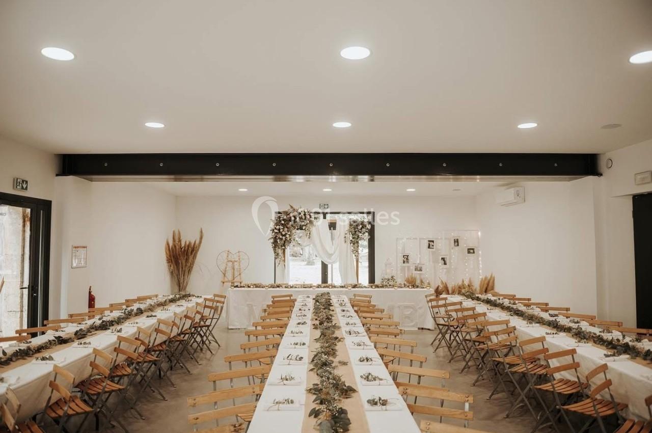 Salle de réception décorée avec des tables alignées, nappes blanches et ornements végétaux, prête pour un événement.