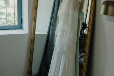 Chambre lumineuse avec lit double, commode en bois, portant à vêtements, télévision et poutre apparente au plafond.