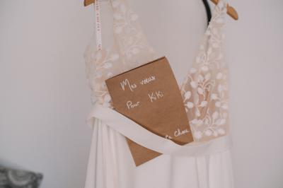 Chambre lumineuse avec lit double, commode en bois, portant à vêtements, télévision et poutre apparente au plafond.