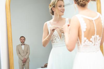 Chambre lumineuse avec lit double, commode en bois, portant à vêtements, télévision et poutre apparente au plafond.