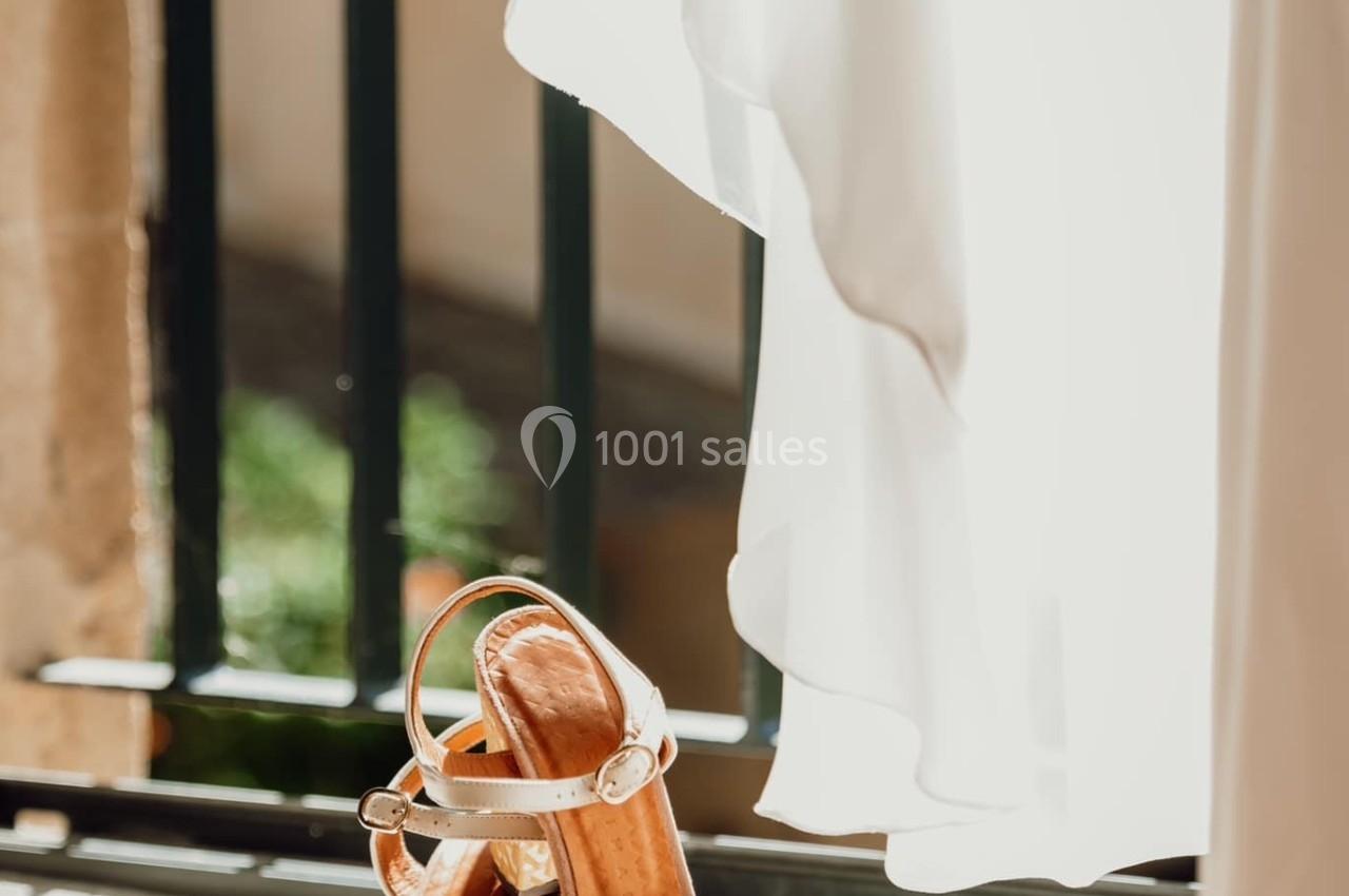 Des sandales dorées posées sur un rebord de fenêtre, éclairées par la lumière naturelle filtrant à travers un rideau blanc.