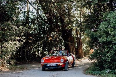 Chambre lumineuse avec lit double, commode en bois, portant à vêtements, télévision et poutre apparente au plafond.