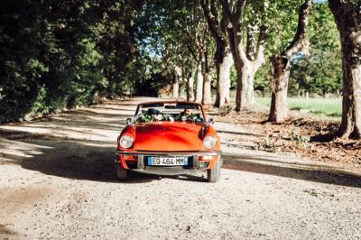 Chambre lumineuse avec lit double, commode en bois, portant à vêtements, télévision et poutre apparente au plafond.