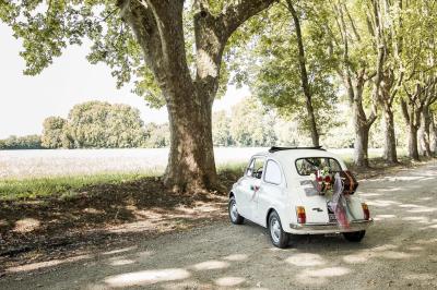Chambre lumineuse avec lit double, commode en bois, portant à vêtements, télévision et poutre apparente au plafond.