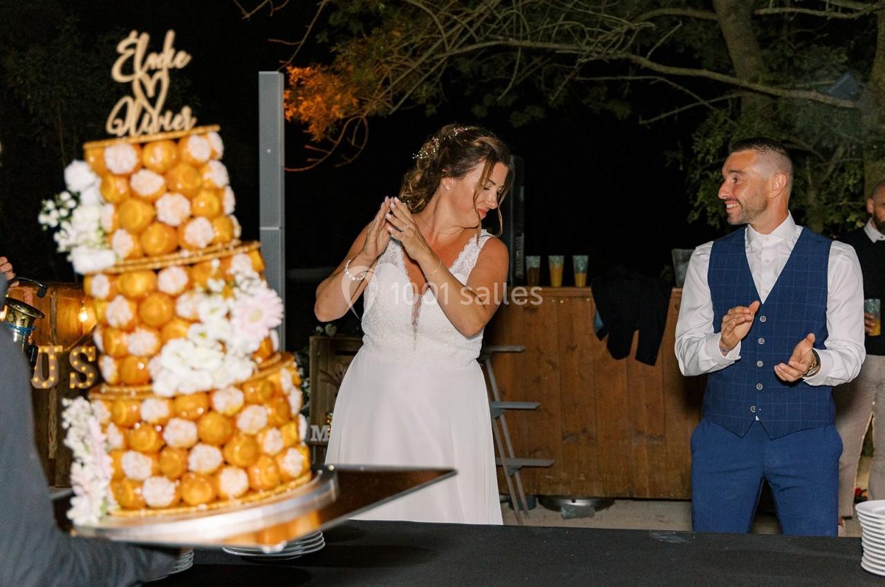 Une mariée et un marié souriants près d'une pièce montée décorée de fleurs, lors d'une réception en extérieur.