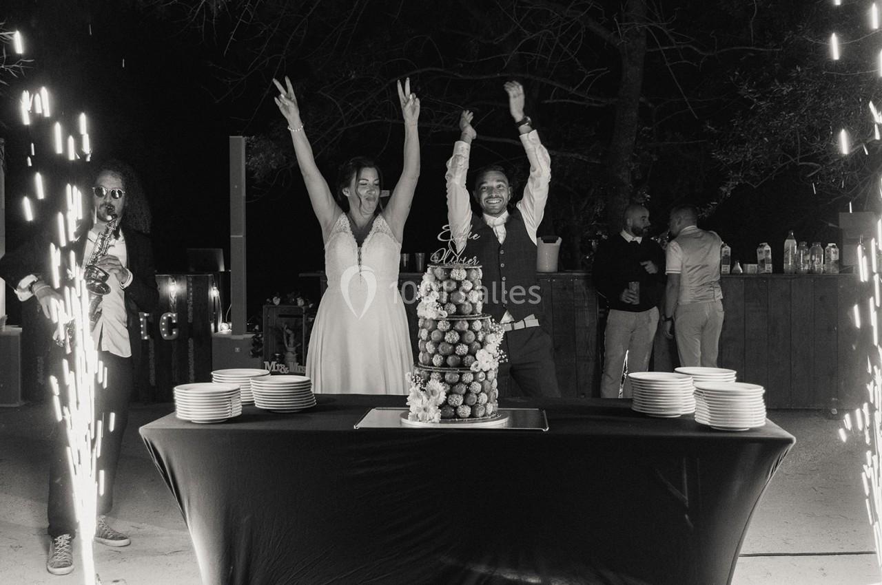 Un couple célèbre son mariage devant une pièce montée, entouré d'invités et d'effets pyrotechniques.