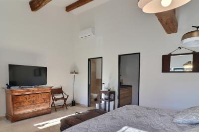 Chambre lumineuse avec lit double, commode en bois, portant à vêtements, télévision et poutre apparente au plafond.