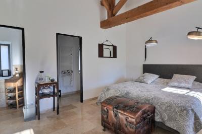 Chambre lumineuse avec lit double, commode en bois, portant à vêtements, télévision et poutre apparente au plafond.