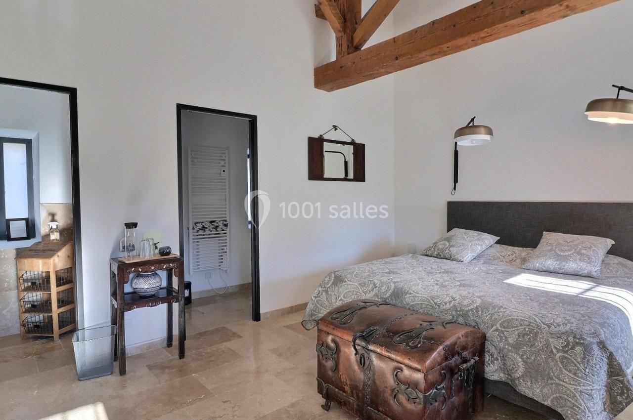 Chambre lumineuse avec lit double, poutres apparentes, sol en pierre et mobilier rustique.