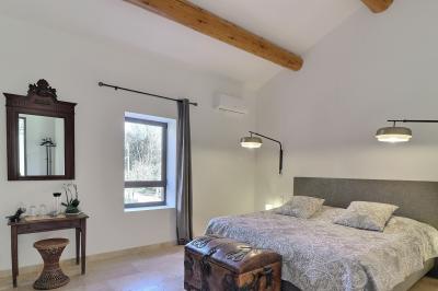 Chambre lumineuse avec lit double, commode en bois, portant à vêtements, télévision et poutre apparente au plafond.