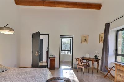 Chambre lumineuse avec lit double, commode en bois, portant à vêtements, télévision et poutre apparente au plafond.