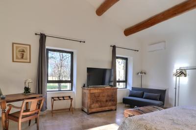 Chambre lumineuse avec lit double, commode en bois, portant à vêtements, télévision et poutre apparente au plafond.