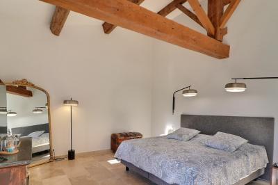 Chambre lumineuse avec lit double, commode en bois, portant à vêtements, télévision et poutre apparente au plafond.