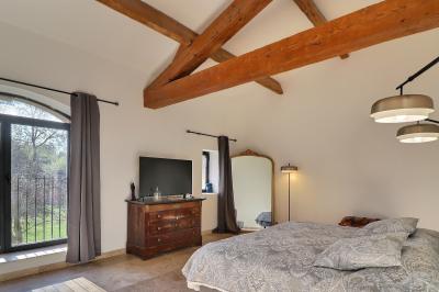 Chambre lumineuse avec lit double, commode en bois, portant à vêtements, télévision et poutre apparente au plafond.