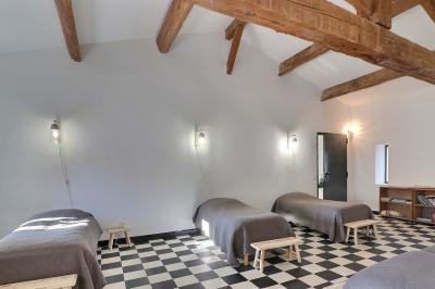 Chambre lumineuse avec lit double, commode en bois, portant à vêtements, télévision et poutre apparente au plafond.