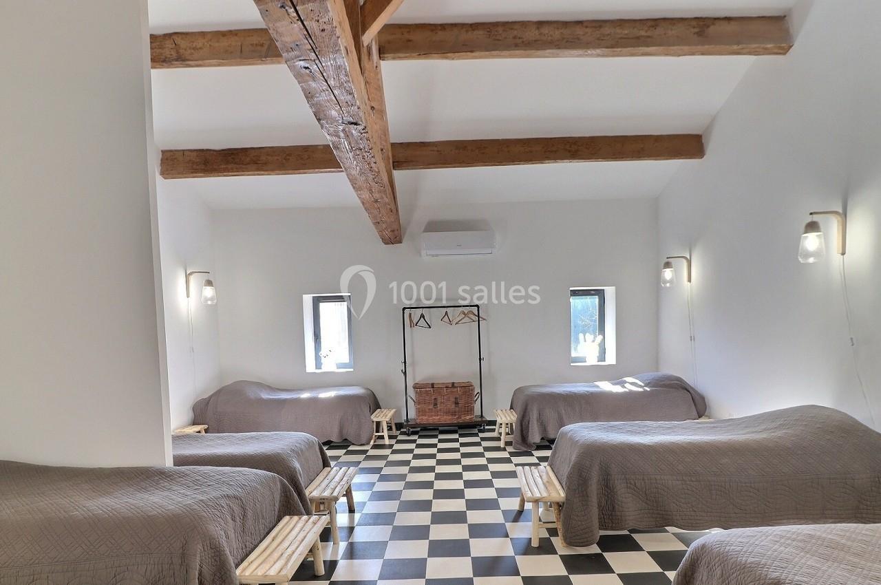 Salle lumineuse avec plafond à poutres apparentes, lits simples alignés, sol en damier noir et blanc.