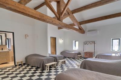 Chambre lumineuse avec lit double, commode en bois, portant à vêtements, télévision et poutre apparente au plafond.