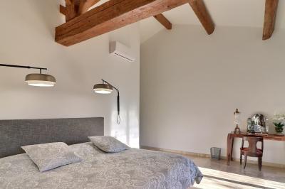 Chambre lumineuse avec lit double, commode en bois, portant à vêtements, télévision et poutre apparente au plafond.